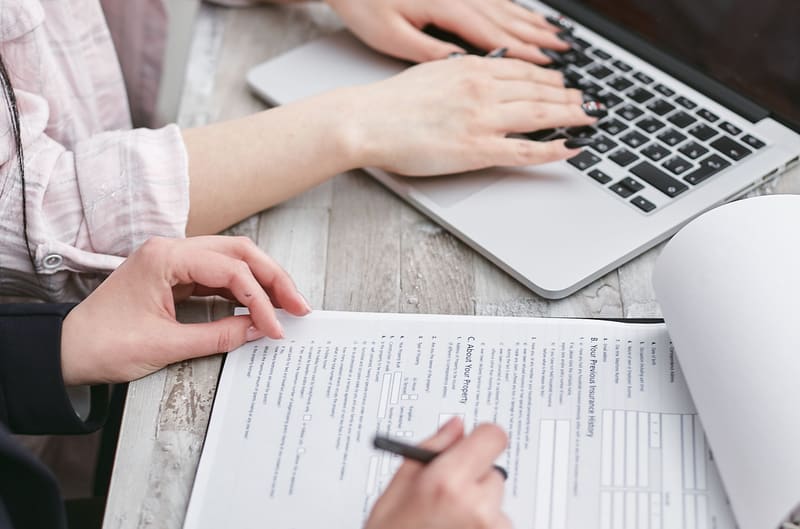 Someone filling in a form with a pen next to a laptop