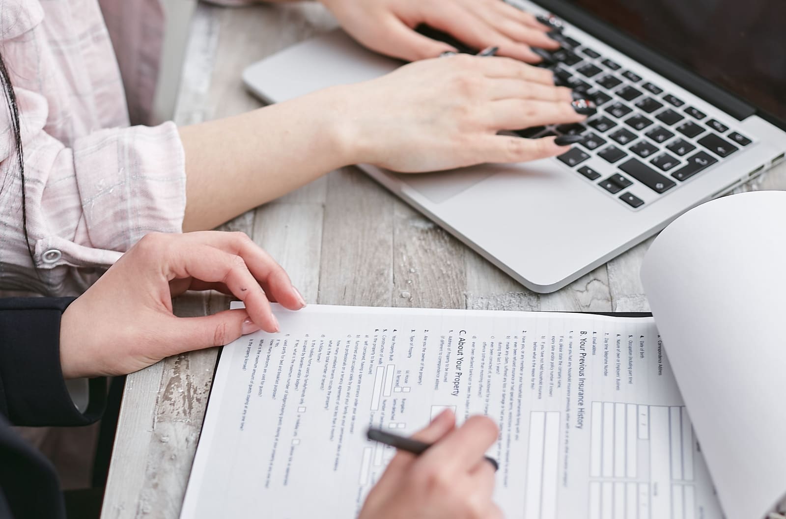 Someone filling in a form with a pen next to a laptop